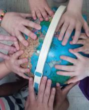 Children's hands rest on a globe they surround.