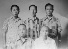 In an aging black and white photo taken sometime around the Korean War, four Korean brothers and their older father face the camera for a formal photo.
