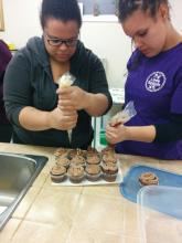Two young people learning to cook, work on their cupcakes.