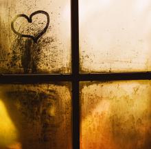 A cross and heart image is seen in a back-lit window with yellow and brown tones.