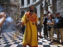 An Eastern Orthodox priest in an orange robe swings a censor in The Church of the Holy Sepulchre in Jerusalem.