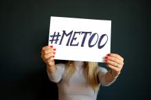 A white woman with blond hair holds a sign saying "#MeToo" in front of her face. 