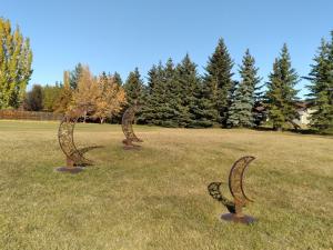 Three metal statues of crescent moons in a field on a nice summer day. 