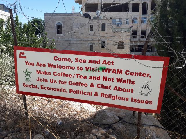   A welcome sign for Wi'am Center on a barbed-wire fence in Palestine, with the message, "Make Coffee/Tea and Not Walls."