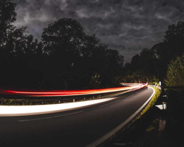 In a long exposure photo, headlights and taillights of cars blur as they rush around a corner at night.