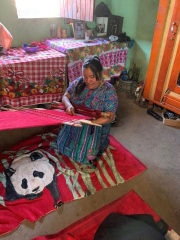 A Guatemalan woman sits weaving red cloth in her home