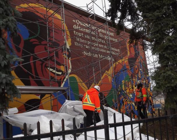 A photo of the large mural of Nelson Mandela on the outside wall of Union United Church in Montreal, just after it was unveiled. It features a large image of Mandela smiling and lifting his arm, along with a quote from him.