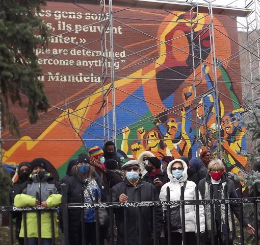 A diverse group of artists and congregation member stand before the huge Mandela mural just after unveiling. They are bundled up against the cold and wearing pandemic masks.