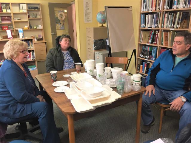 A group of three people meet to discuss the church's recyclable food wares. The recyclable dishes and cups are on the table before them.
