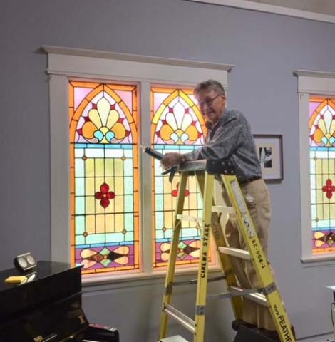 A man on a step ladder caulks a colourful stained glass window at the church.