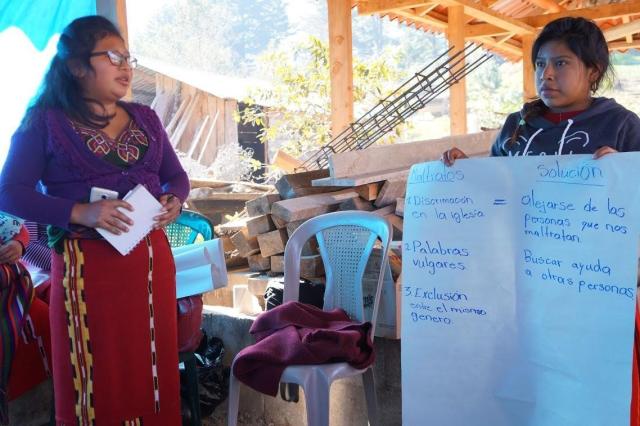 Two Guatemalan women, one holding up a large sheet of paper with Spanish writing on it, make a presentation.