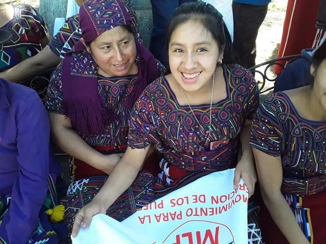 Two women in the traditional woven dress of women from Nebaj, Guatemala, show of some of the produce they grew using new agricultural skills.