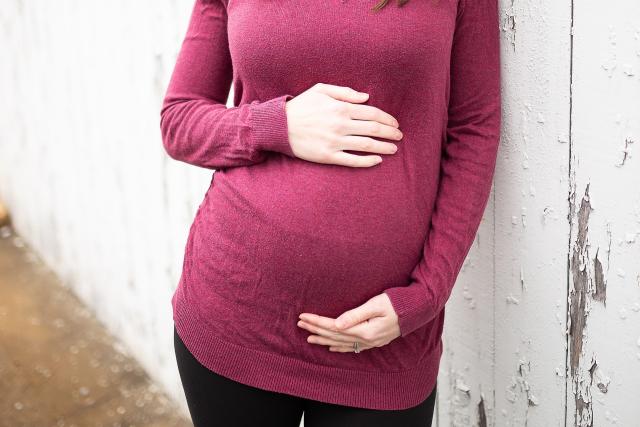 A pregnant woman in a red top standing next to a wooden fence.