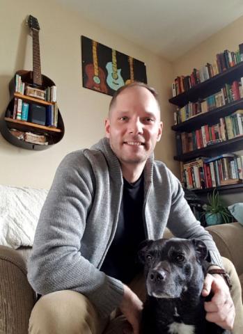 A photo of Jesse smiling in his home, with his dog.