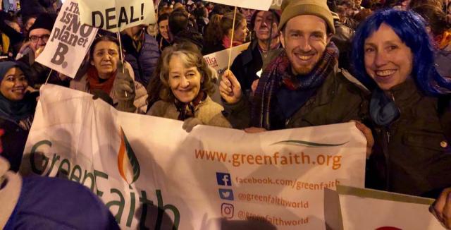 Wendy Evans and a group of enthusiastic people hold a GreenFaith banner at a night rally 