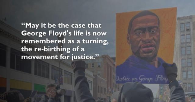 A person in a crowd on the street holds up a painting of George Floyd