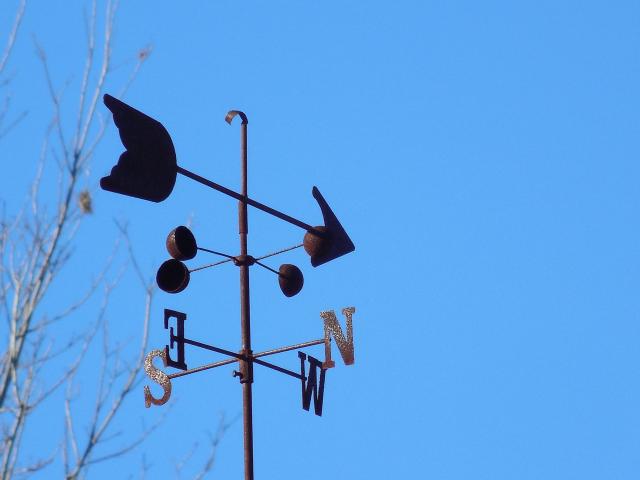 Metal weather vane made up of an arrow and north, south, east, west arrows against a blue sky