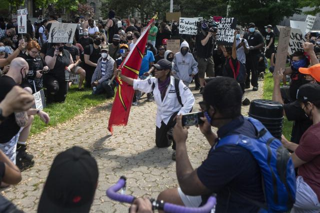 A man with a red Mohawk First Nations flag kneels in solidarity at a Black Lives Matter protest in Toronto, June 2020.