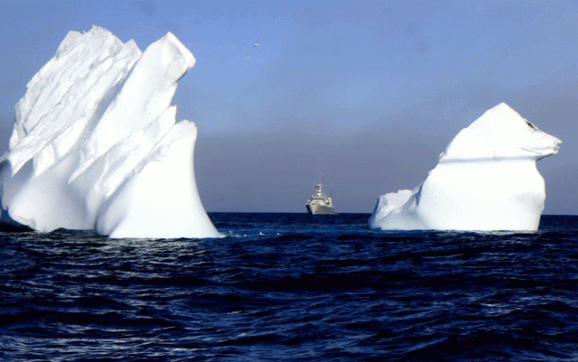 A navy vessel makes its way between two huge icebergs.