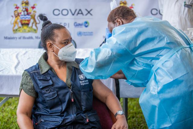 A woman wearing a World Health Organization vest receives a COVID vaccine from a nurse