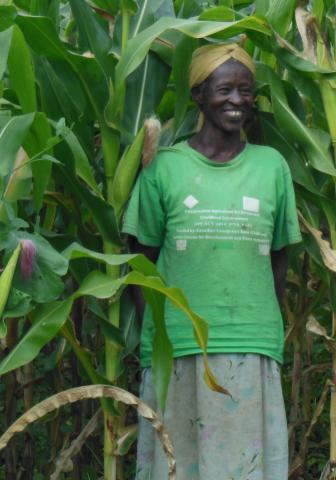 A smiling woman stands among tall plants in a farm field.