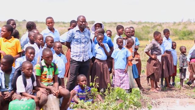 Emmanuel Baya stands in a Kenyan field surrounded by children.