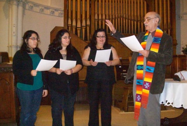 A male minister with a colourful stoll, offers a prayer to welcome three women who are becoming members of the congregation.