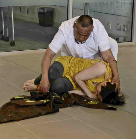 A photo from the performance of The Sunflower Man, featuring two Latinx dancers. In this photo, the woman in a yellow dress is a dying sunflower, while the man dressing in all white, is the sun holding her close.