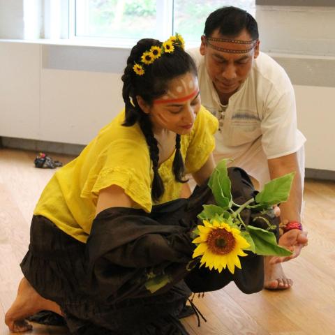 A photo of two Latinx performers, dressing in traditional farmworker clothes, cradling a sunflower during a show.
