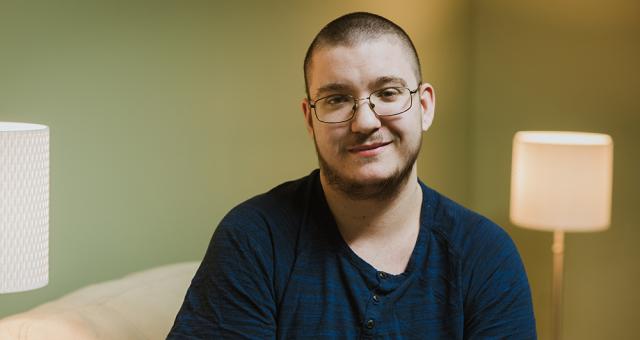 Image: Head shot of a man wearing glasses and a dark blue shirt in a room with pale green walls.