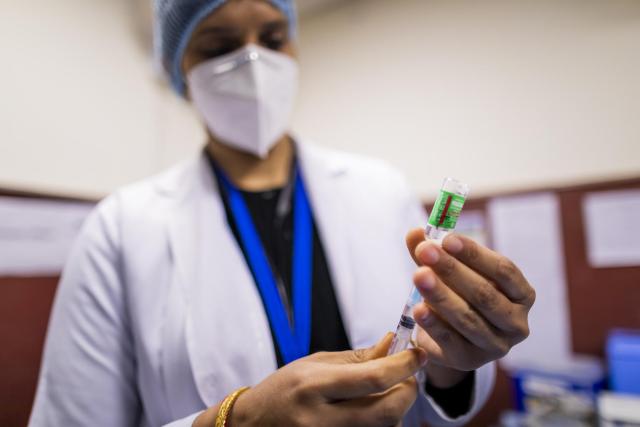 Image: A woman wearing a lab coat and face mask fills a syringe from a vaccination bottle.