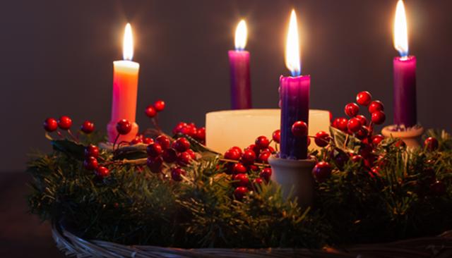 Coloured advent candles arranged in a pine wreath.