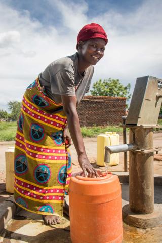 A woman in Africa fills a large orange water barrel from a tap