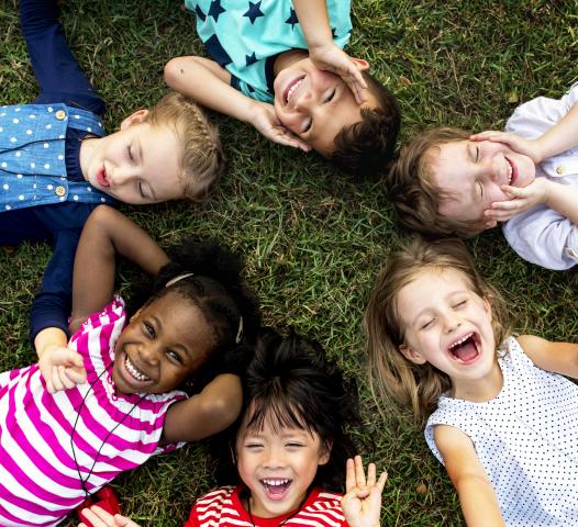 A diverse group of kids smile together while laying in a circle at a playground.