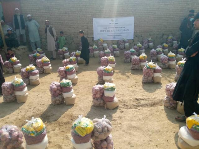 Afghan men and boys keep on eye on rows of bundles of food lined up on the ground in front of a wall.