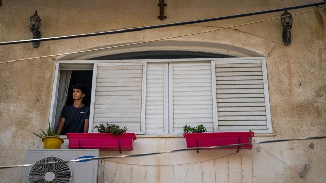 A teenage boy stands in the window of a stone house in Palestine.