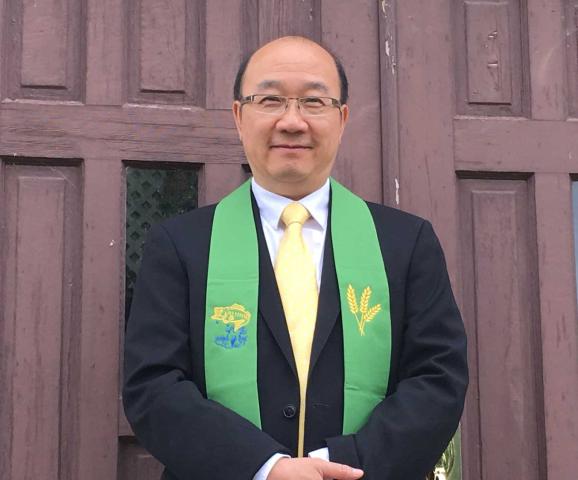 Ministry personnel Calin Chun-hong Lau, a man of Chinese descent, stands before a church door in a suit and green stole.