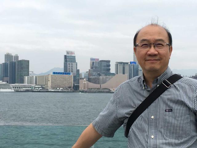 Calin Chun-hong Lau poses in front of the port at Hong Kong, dressed casually, in what appears to be a visit to the city he grew up in.