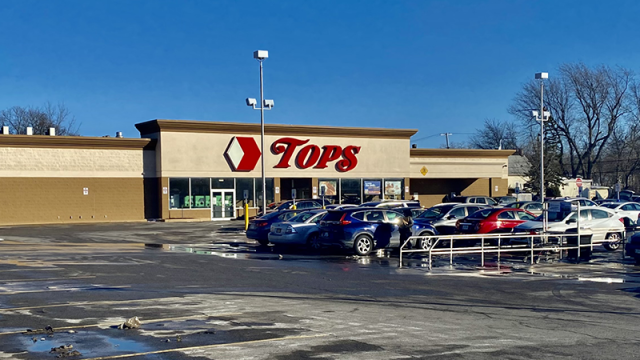 Exterior of a supermarket with the name Tops in large red letters over the doors and cars parked in front. 
