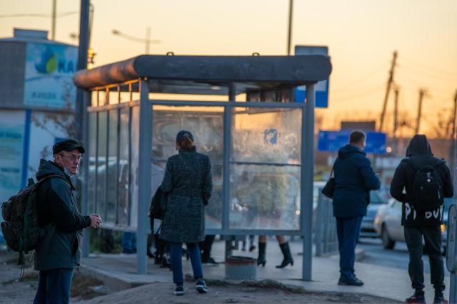People stand around a bus shelter at sunset.