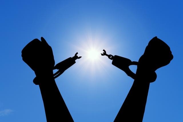 A pair of arms rise in triumph against a blue sky, breaking the chains of enslavement.