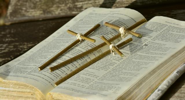 An open Bible with three crosses made of twigs lying across it.