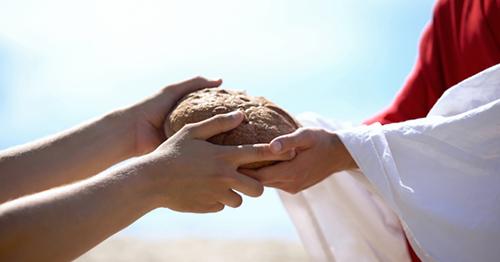 Hands that look like Jesus' hold out bread to another person's hands.