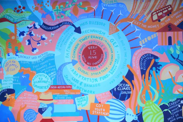 A multicoloured mural of people, words, trees, wind turbines, and more has as its centre a red circle with the words Keep 1.5 Alive painted on it.