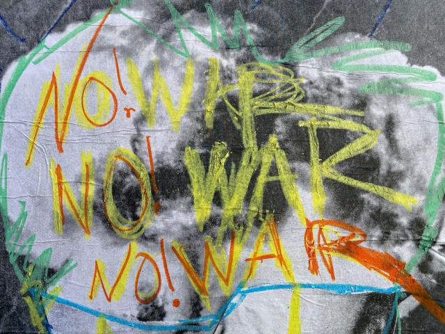 The words No! War are painted three times in yellow and orange on a wall.