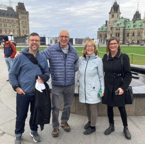 A group shot of the four members of the Hunger on the Hill team, standing outside with the Parliament Building in Ottawa in the background.