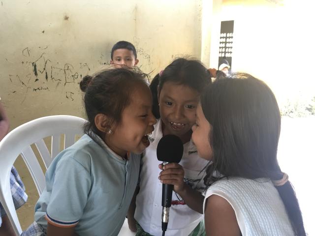 Three laughing little girls crowd around a microphone one is holding while a little boy looks on.