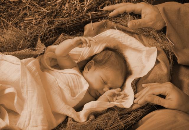 A swaddled infant representing Jesus lies in a wicker basket lined with straw, their parents' hands resting on the edge of the basket.