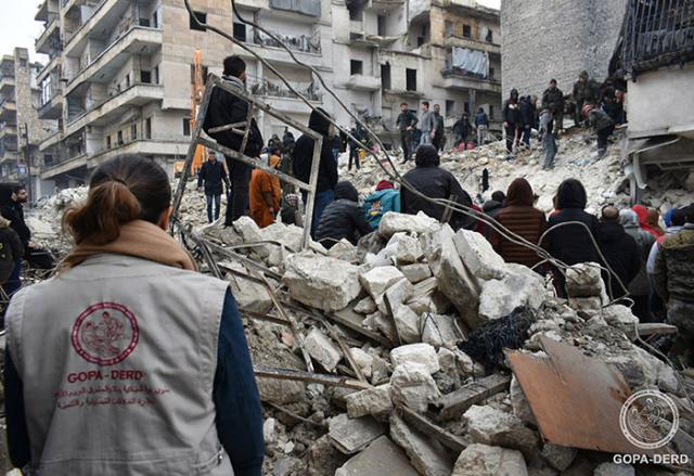 People standing in rubble after an earthquake hits Türkiye (Turkey) and Syria.