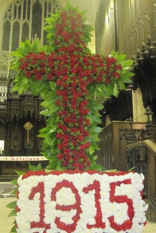 A cross made of flowers and greenery above the date 1915 written in flowers.